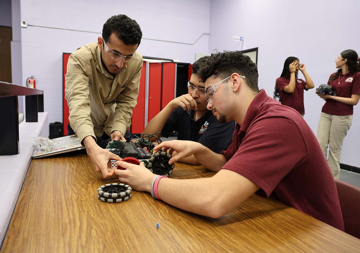 HSA Teacher smiles while kneeling beside a young student in a classroom setting.